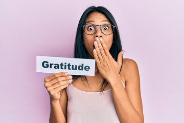 Wall Mural - Young african american woman holding gratitude message paper covering mouth with hand, shocked and afraid for mistake. surprised expression