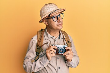 Wall Mural - Middle age bald man wearing explorer hat and vintage camera smiling looking to the side and staring away thinking.