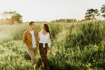 Beautiful young woman and a man walk, hug and kiss in nature at sunset.