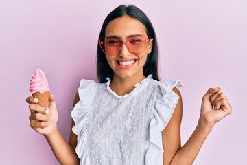 Young brunette woman wearing summer style holding ice cream screaming proud, celebrating victory and success very excited with raised arm