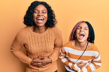 Poster - Beautiful african american mother and daughter wearing wool winter sweater smiling and laughing hard out loud because funny crazy joke with hands on body.