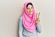 © Krakenimages.com - Young caucasian woman wearing traditional islamic hijab scarf showing and pointing up with fingers number two while smiling confident and happy.