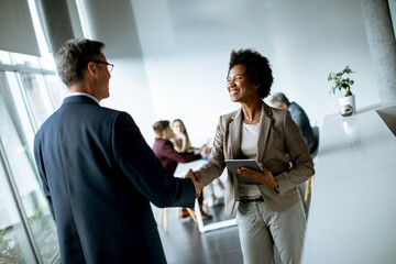 businesswoman holding digital tablet and looking at handsome colleague while shaking hands in office