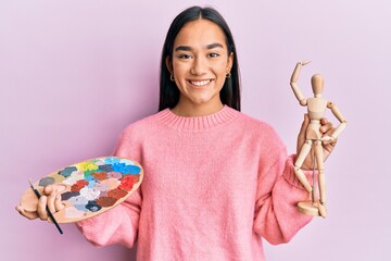 Poster - Young asian woman holding painter palette and art manikin smiling with a happy and cool smile on face. showing teeth.