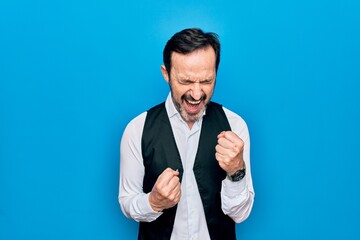 Middle age handsome man wearing elegant shirt and vest over isolated blue background celebrating surprised and amazed for success with arms raised and eyes closed