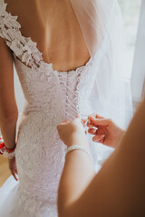 Poster - Vertical shot of a female's hands tying the threads of the bride's dress