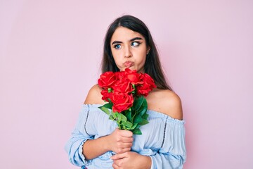 Wall Mural - Brunette teenager girl holding flowers making fish face with mouth and squinting eyes, crazy and comical.