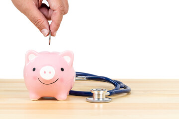 Hand putting depositing money into pink piggy bank with stethoscope on wooden desk on white background, concept financial health check and retirement fund and insurance