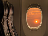 Fototapeta Desenie - Big sun at sunset sky from airplane window. Travelling by airplane seat near window enjoying beautiful sunset. Sunset through aircraft window.
