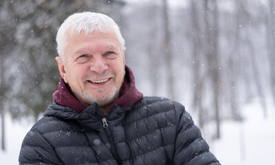 Happy smiling mature man outdoorshooded sweatshirt on snowy winter day on nature background