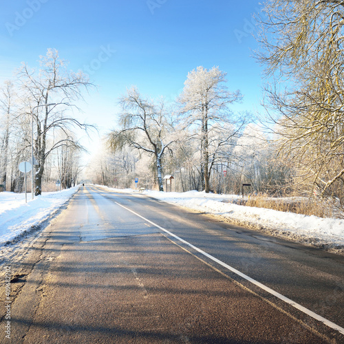 An empty asphalt road after cleaning. Car tracks in a fresh snow. Snow-covered birch forest in the background. Clear blue sky. Winter driving in Finland. Global warming theme