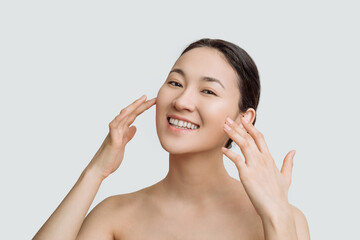 Wall Mural - Skin care. Asian woman with a beautiful face touches a healthy skin portrait. Beautiful smiling Asian girl model with natural makeup moisturized skin on white background close up