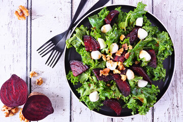 Poster - Healthy kale and beet salad with cheese and walnuts. Top view table scene over a white wood background.