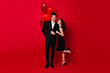 © Look! - Graceful girl standing on one leg and gently touching boyfriend. Studio shot of happy couple posing on red background.