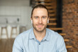 © Face Stock - Portrait of an attractive young bearded hipster man smiling at the camera, wearing headphones, standing in the modern house, wearing a casual shirt. The view while the video-calling concept