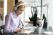 Focused teen student girl wearing headphones, watching webinar or online learning videos on computer, taking notes. Woman studying from home, attending virtual class. Distance education concept