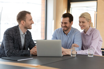 Happy married clients consulting real estate agent in his office. Realtor showing online virtual tour in house on laptop to buyers at meeting in agency. Couple choosing apartment for rent, buying