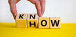 Know how symbol. Businessman turns cubes and changes the word 'how' to 'know'. Beautiful yellow table, white background. Copy space. Business and know how concept.