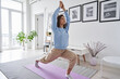 Fit healthy young woman doing pilates yoga exercise fitness training workout at home interior standing in warrior pose. Physical activity for body and mind relaxation, healthy lifestyle habits concept