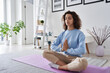 Healthy serene young woman meditating at home with eyes closed doing pilates breathing exercises, relaxing body and mind sitting on floor in living room. Mental health and meditation for no stress.