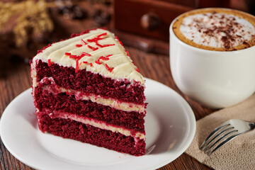 Wall Mural - Slice of red velvet cake on a plate with a cappuccino on a wooden table