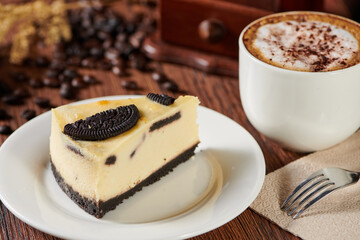 Poster - Slice of cheesecake with chocolate sandwich cookies and cappuccino on a wooden table