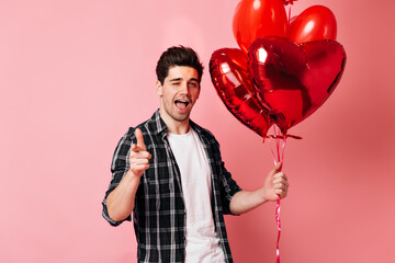 Wall Mural - Happy young man posing in valentine's day in studio. Caucasian guy in checkered shirt holding helium balloons.