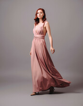 Bridesmaid's Look In Dust Pink. Young Ginger Woman In Summer Transformer Evening Dress And High Heel Shoes On Grey Background At Studio. Gorgeous Sexy Lady.