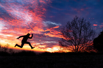 Fondo de atardecer rojo y azul con un arbol y la silueta de un hombre saltando corriendo 