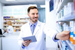 © littlewolf1989 - Handsome male pharmacist in white coat working in pharmacy store or drugstore. Checking medicines on his tablet computer. Healthcare and apothecary.