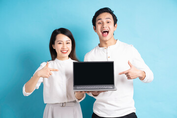 Canvas Print - Portrait of happy young couple using laptop on blue background