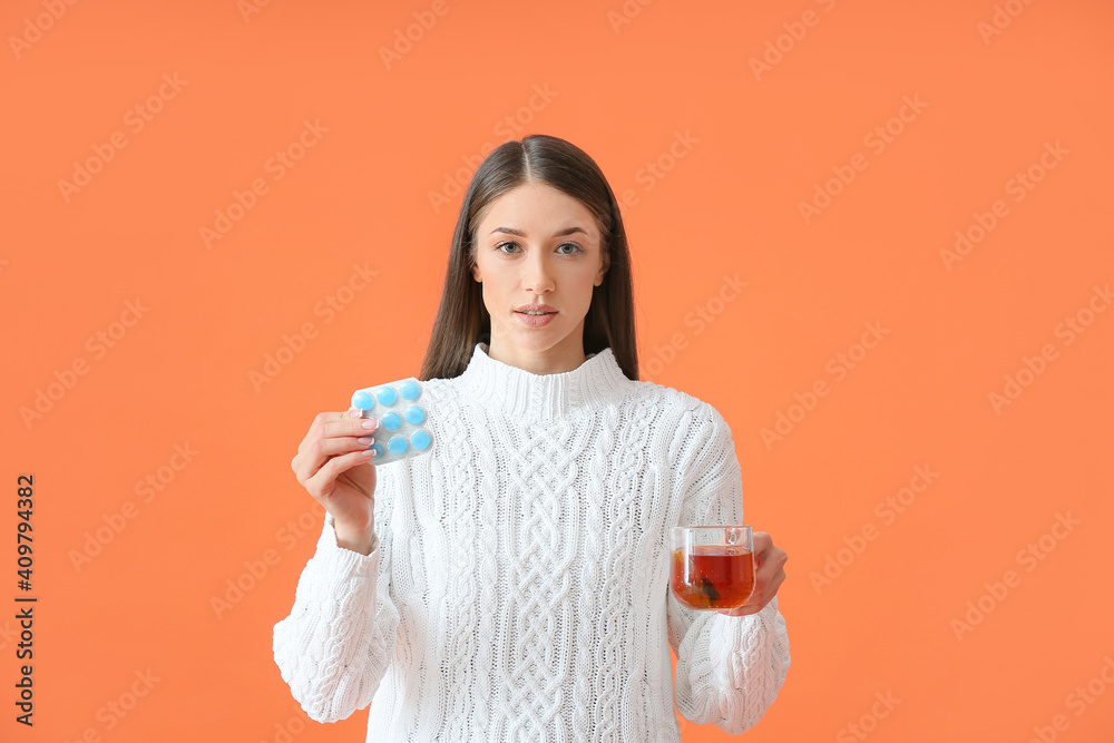 Sick young woman with tea and pills on color background