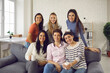 © Studio Romantic - Group of young women sitting on sofa at home, drinking tea, smiling and looking at camera. Happy friends and coworkers enjoying Casual Friday at work and spending coffee break on modern office couch