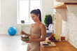 Slender fitness woman in sportswear standing at home in the kitchen with a bowl of fresh salad. Happy woman enjoys healthy food after workout. Fitness, dieting and healthy lifestyle concept.