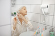 © zinkevych - Gray-haired woman brushing her hair in the bathroom