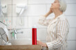 © zinkevych - Gray-haired woman in pajama doing hair in the bathroom