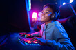 Professional Streamer African young woman cyber gamer studio room with personal computer armchair, keyboard in neon color blur background