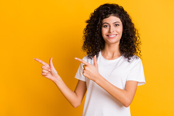 Wall Mural - Photo portrait of curly brunette pointing finger blank space isolated on vibrant yellow color background