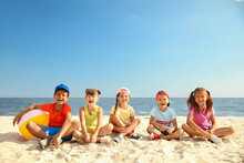 Group Of Happy Children Sitting On Sand At Sea Beach. Summer Camp