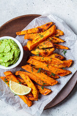 Wall Mural - Baked sweet potato wedges with guacamole on wooden plate, gray background. Vegan food concept.