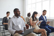 © Seventyfour - Multi-ethnic group of people sitting on chairs in audience at business conference or seminar and taking notes, copy space