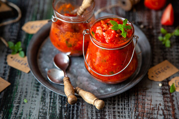 homemade red tomato sauce in glass jar on metal plate on wooden table with basil leaves