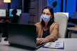 © DC Studio - Overworked businesswoman wearing face mask as safety precautiond due to company ruless. Woman following social distancing rules due to coroanvirus pandemic while working late hours at the office.