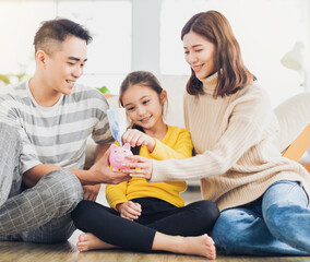 Wall Mural - Father, mother and daughter holding a piggy bank and money  at home. Family and saving for future concept.