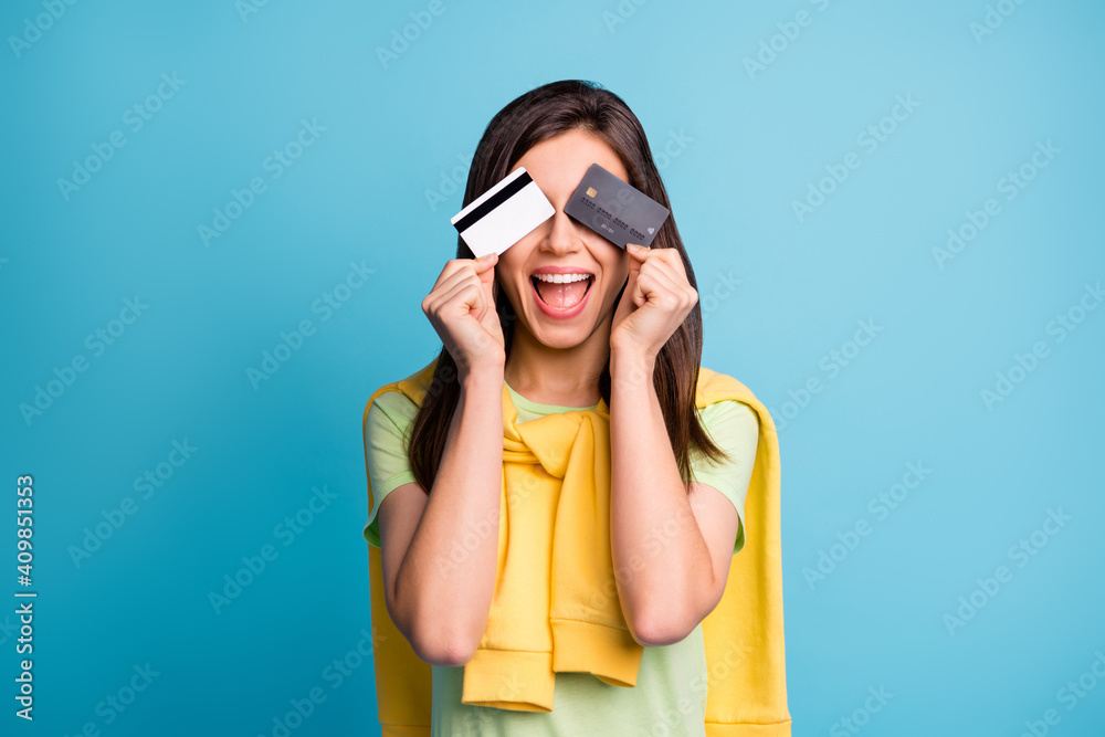 Photo of young attractive pretty crazy excited smiling girl cover eyes with two credit cards isolated on blue color background - obrazy, fototapety, plakaty 