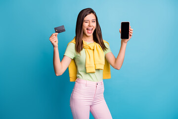 Canvas Print - Photo of young beautiful crazy excited smiling woman girl wink eye show credit card phone isolated on blue color background