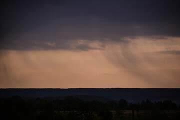 rain seen from afar at sunset. colored clouds on the horizon