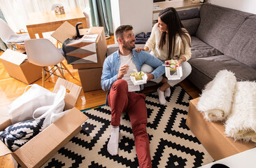 Wall Mural - Smiling young couple move into a new apartment, sitting in the living room eating and taking a break from unpacking.