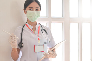 A woman doctor wearing a mask holds a patient file with stethoscope.