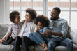 © fizkes - Close up happy African American family relaxing on cozy couch, smiling mother and happy father wearing glasses hugging adorable little daughter and son, sitting on sofa, enjoying leisure time